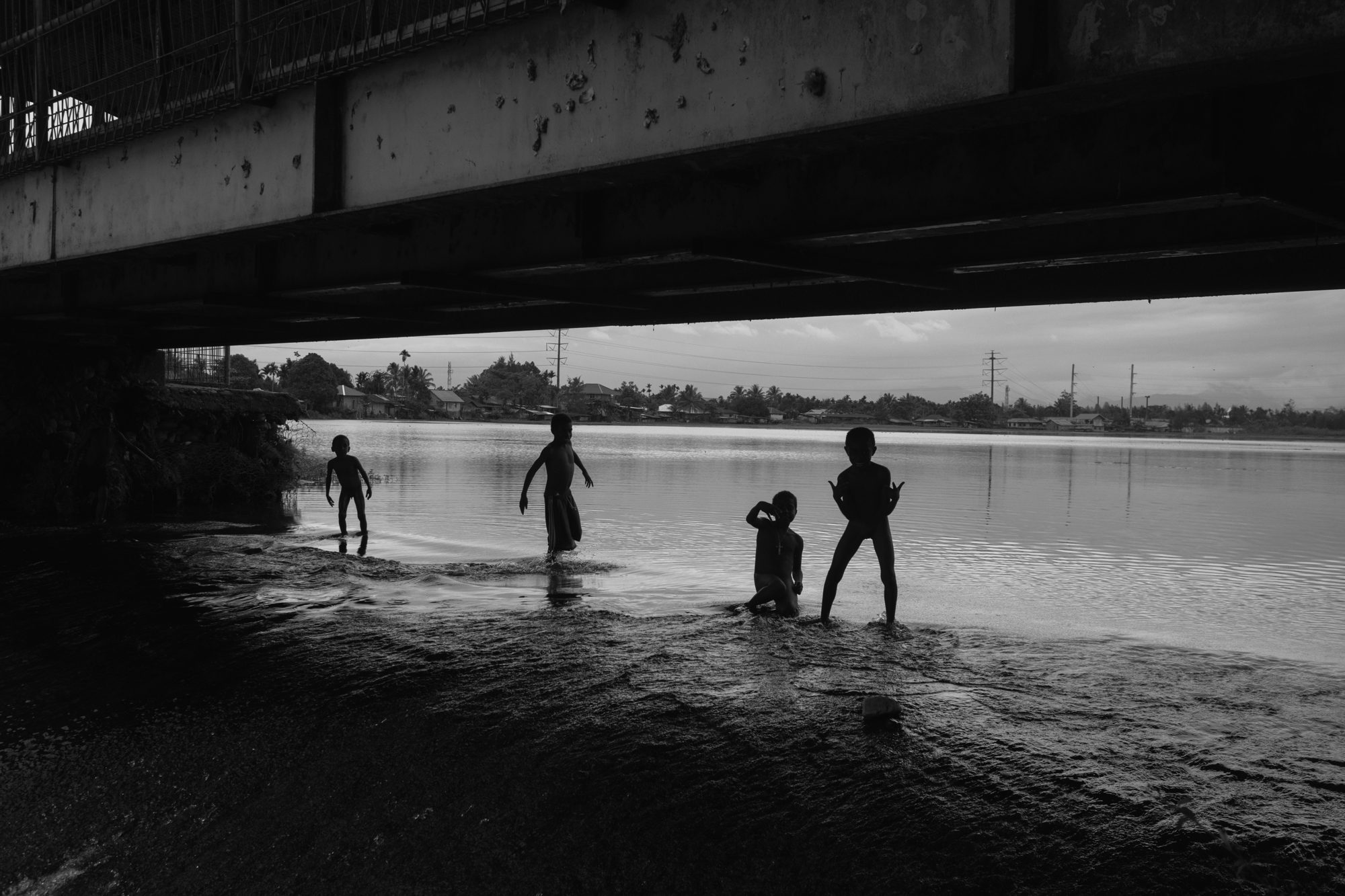 Children play beneath a bridge at dusk, in black and white
